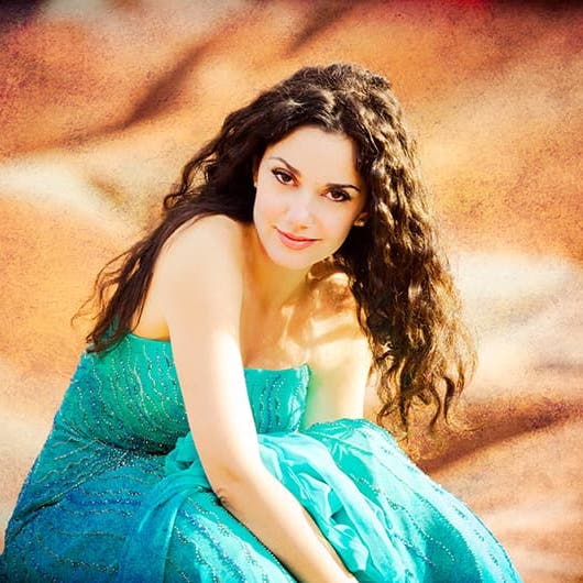 Miriam is wearing a blue dress and sitting on what appears to be sand dunes.